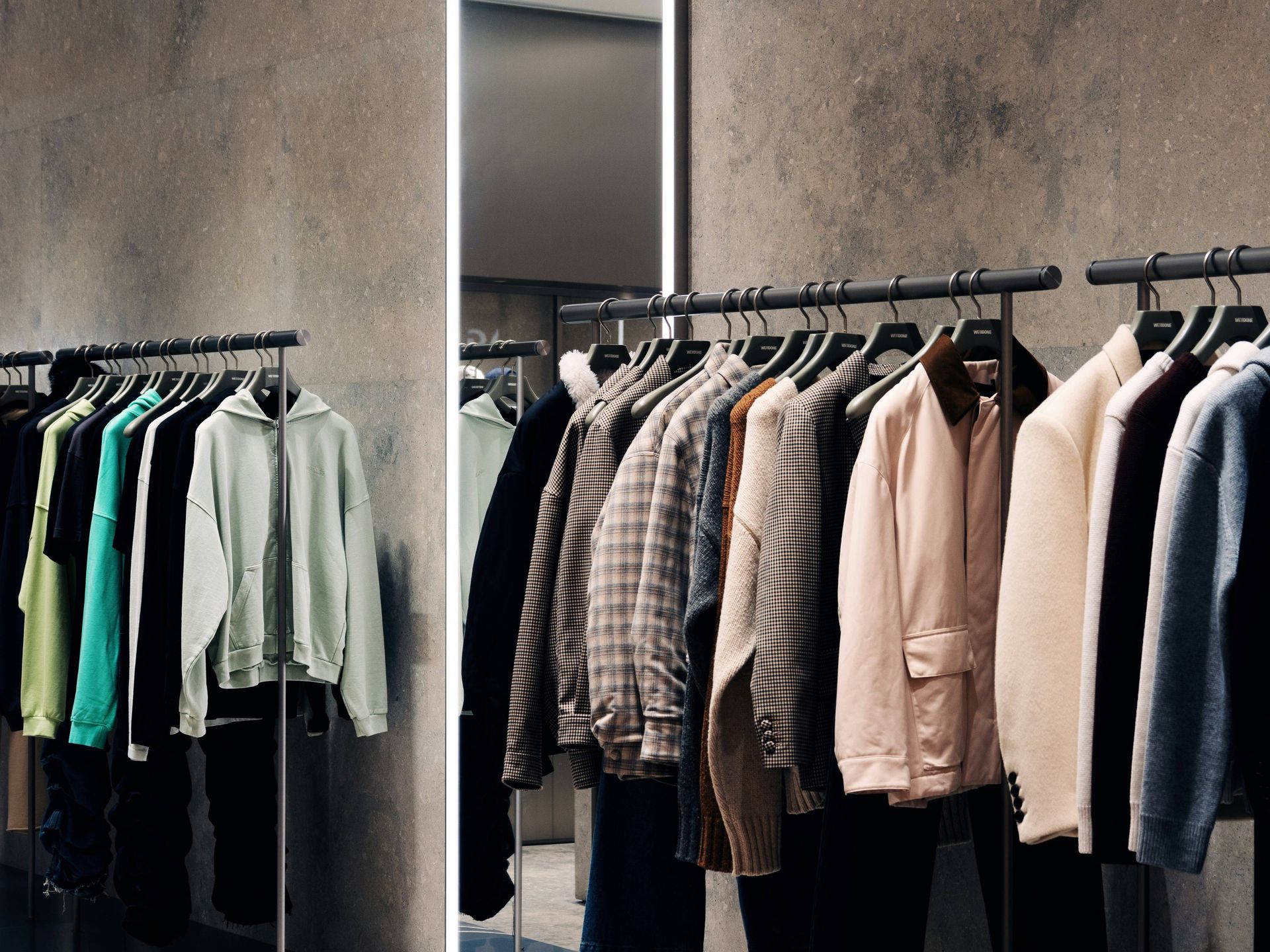 Moderne Boutique mit ordentlich aufgehängter Herrenbekleidung in neutralen Farbtönen an Kleiderstangen.
