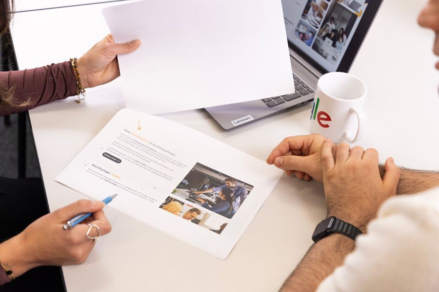 Eine Frau hält ein Blatt Papier vor einen Laptop.