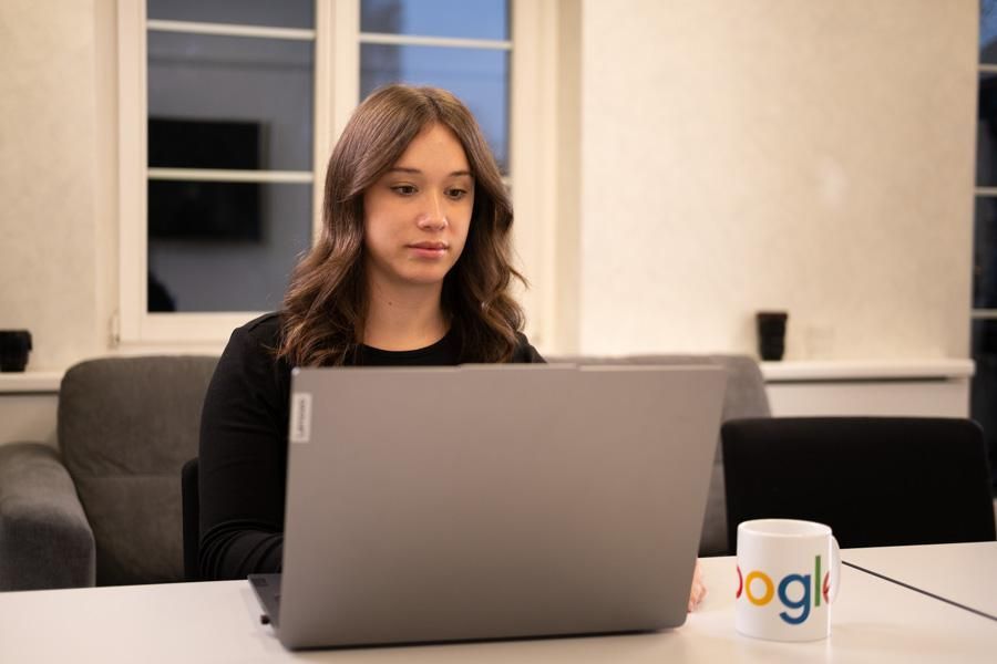 Eine Frau sitzt hinter einem grauen Laptop und arbeitet

