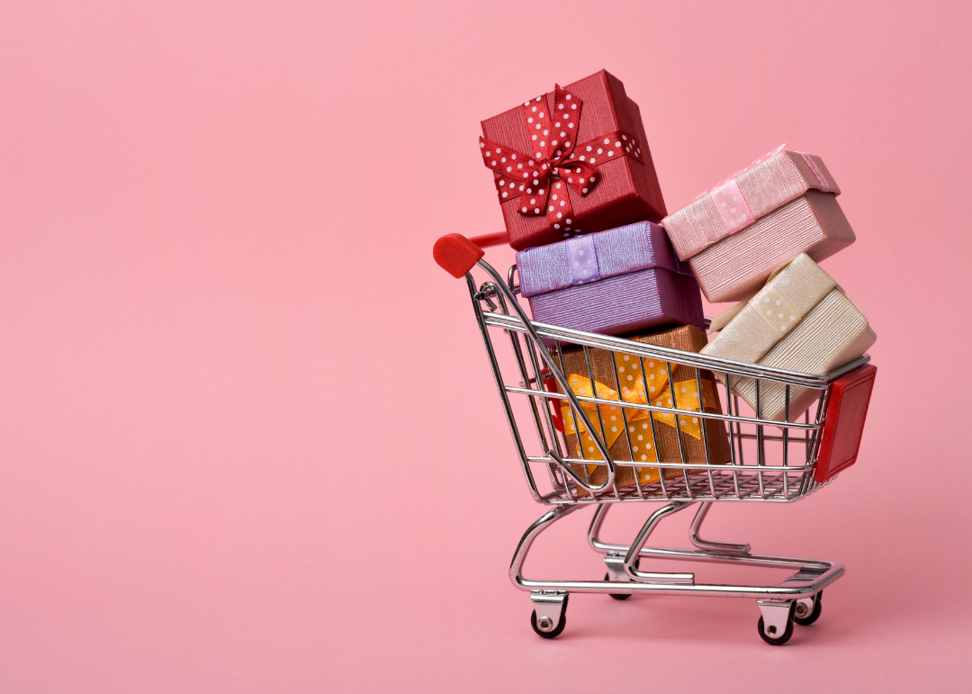 Ein Einkaufswagen gefüllt mit Geschenken steht vor einem rosa Hintergrund