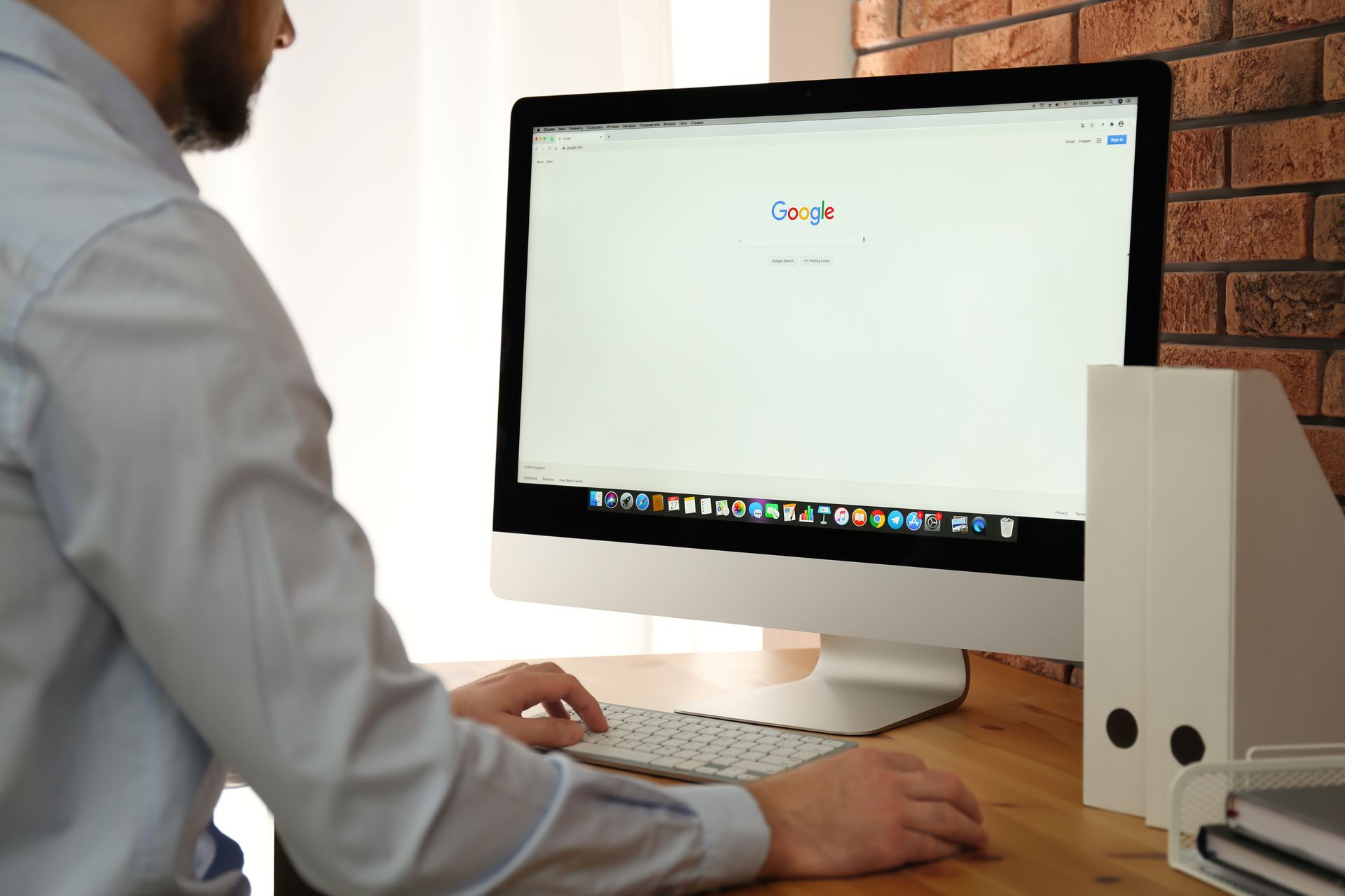 Eine Person, die an einem Holzschreibtisch einen Desktop-Computer benutzt, auf dessen Bildschirm Google geöffnet ist.