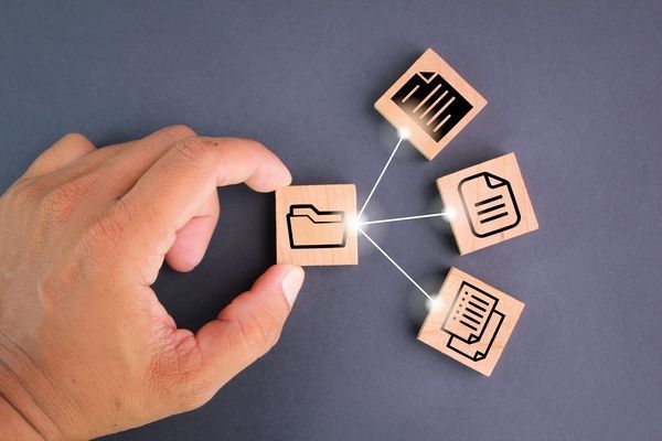 Eine Hand, die ein Ordnersymbol, das mit drei Dokumentsymbolen verbunden ist, auf einen hellen Hintergrund legt.