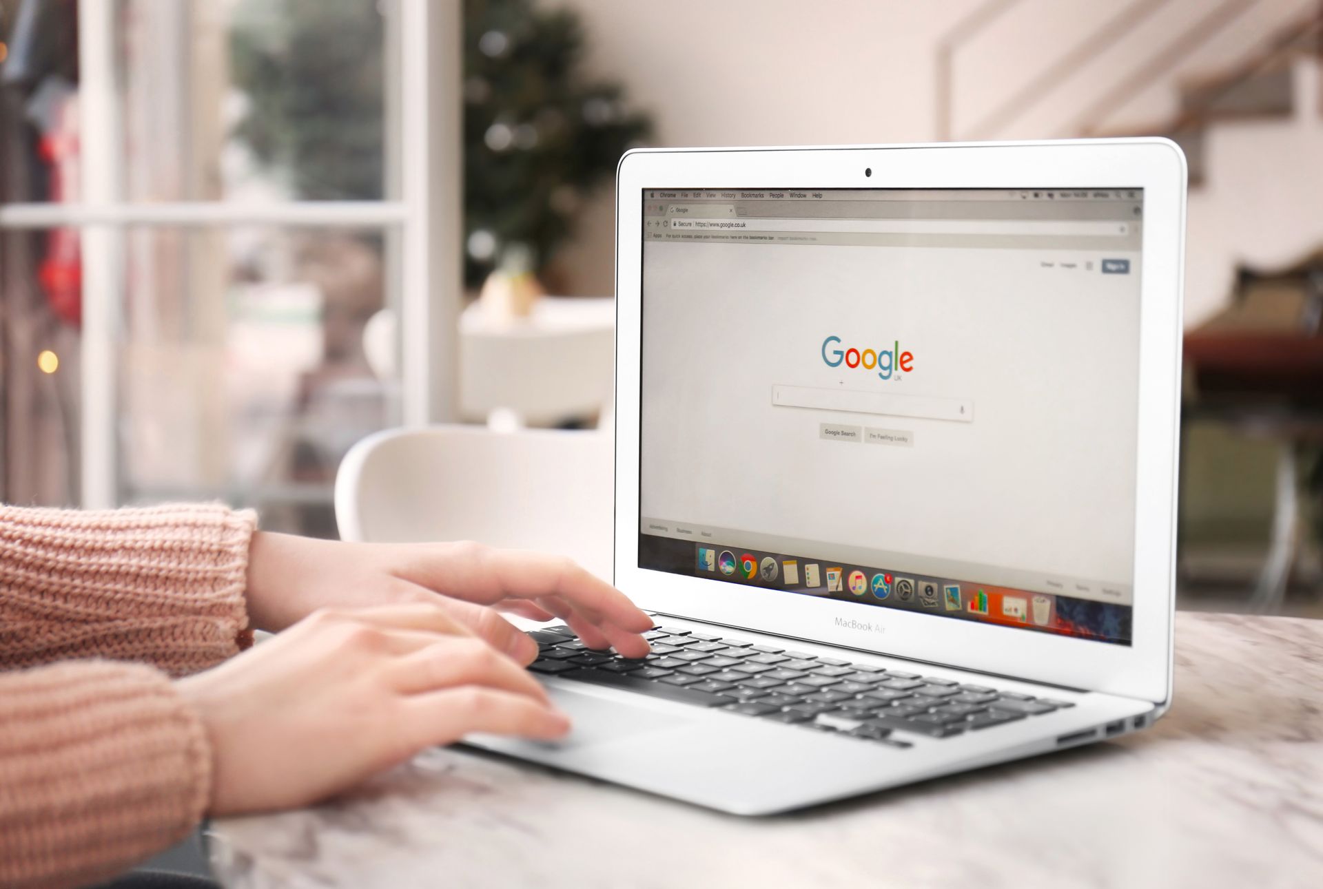 Person, die auf einem Laptop tippt, auf dem die Google-Startseite geöffnet ist, in Innenräumen.