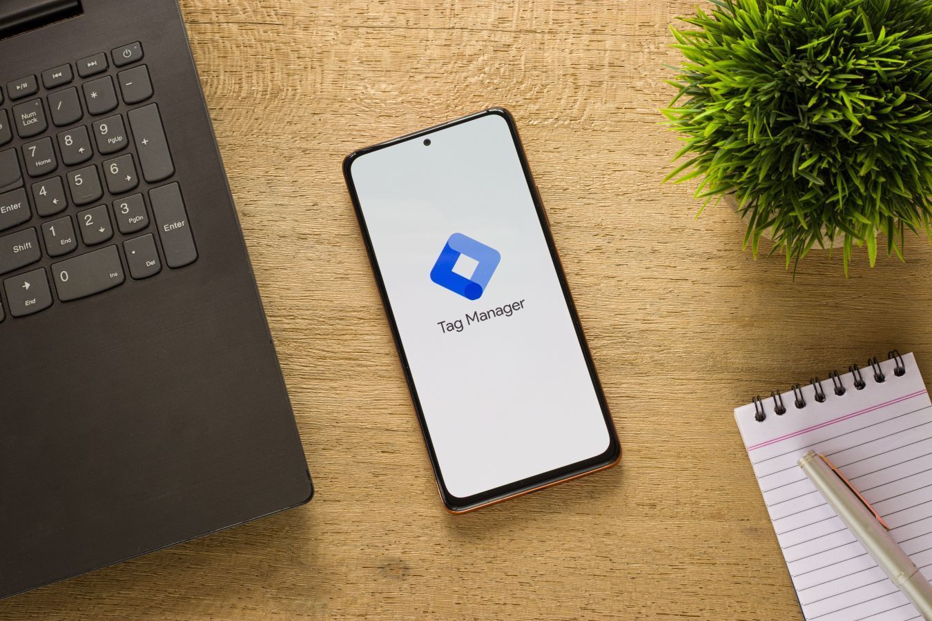 A cell phone is sitting on a wooden table next to a laptop and a notebook.
