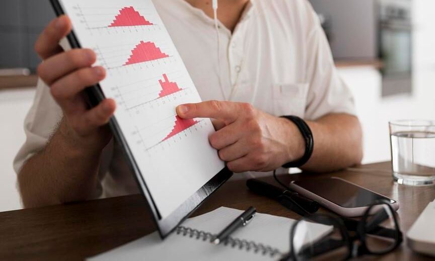 A man is sitting at a table holding a tablet and pointing at a graph.