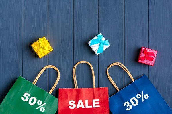 Verkaufstaschen mit den Aufschriften „50 %“, „SALE“ und „30 %“ sowie drei Geschenkboxen auf blauem Hintergrund.
