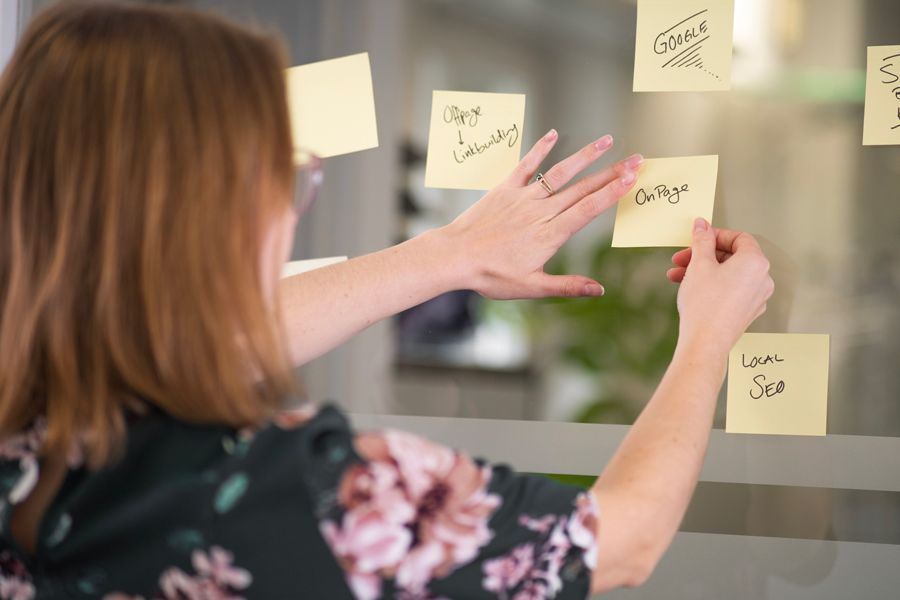 Eine Frau steht hinter einer Glasscheibe und schreibt auf gelbe Post-Its
