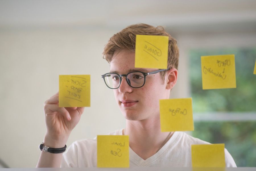 Eine Frau steht hinter einer Glasscheibe und schreibt auf gelbe Post-Its