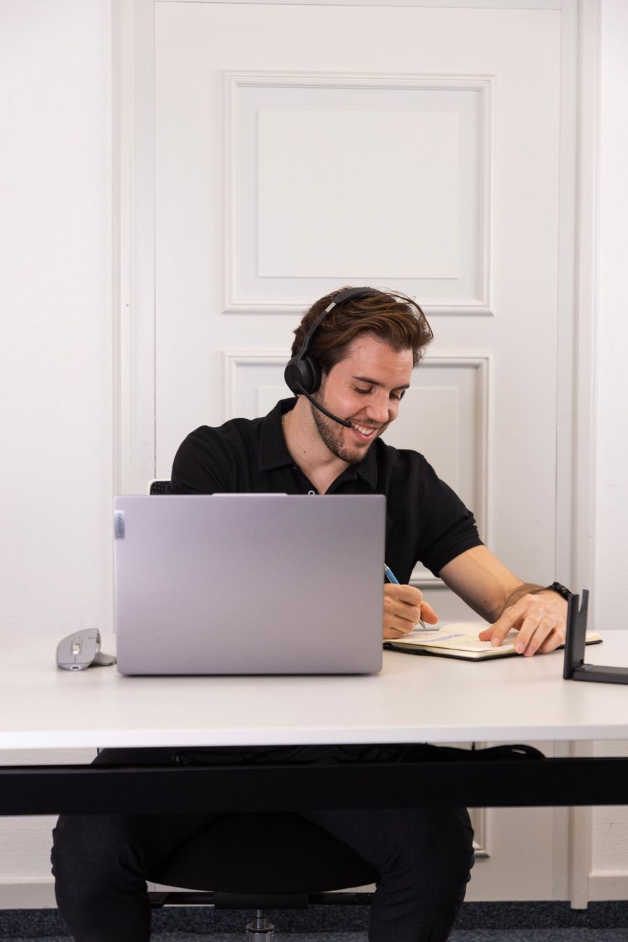 Eine Mann sitzt an einem Tisch und benutzt einen Laptop mit Kopfhörer.