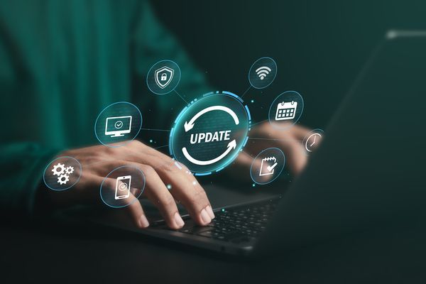 Hände, die auf einem Laptop tippen, auf dem ein leuchtendes „UPDATE“-Symbol und technische Symbole vor einem dunklen Hintergrund zu sehen sind.