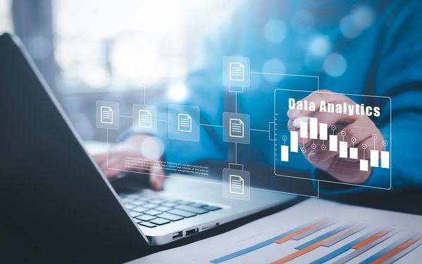 Hände, die auf einem Laptop tippen, während Grafiken und Diagramme zur digitalen Datenanalyse auf dem Bildschirm eingeblendet werden.
