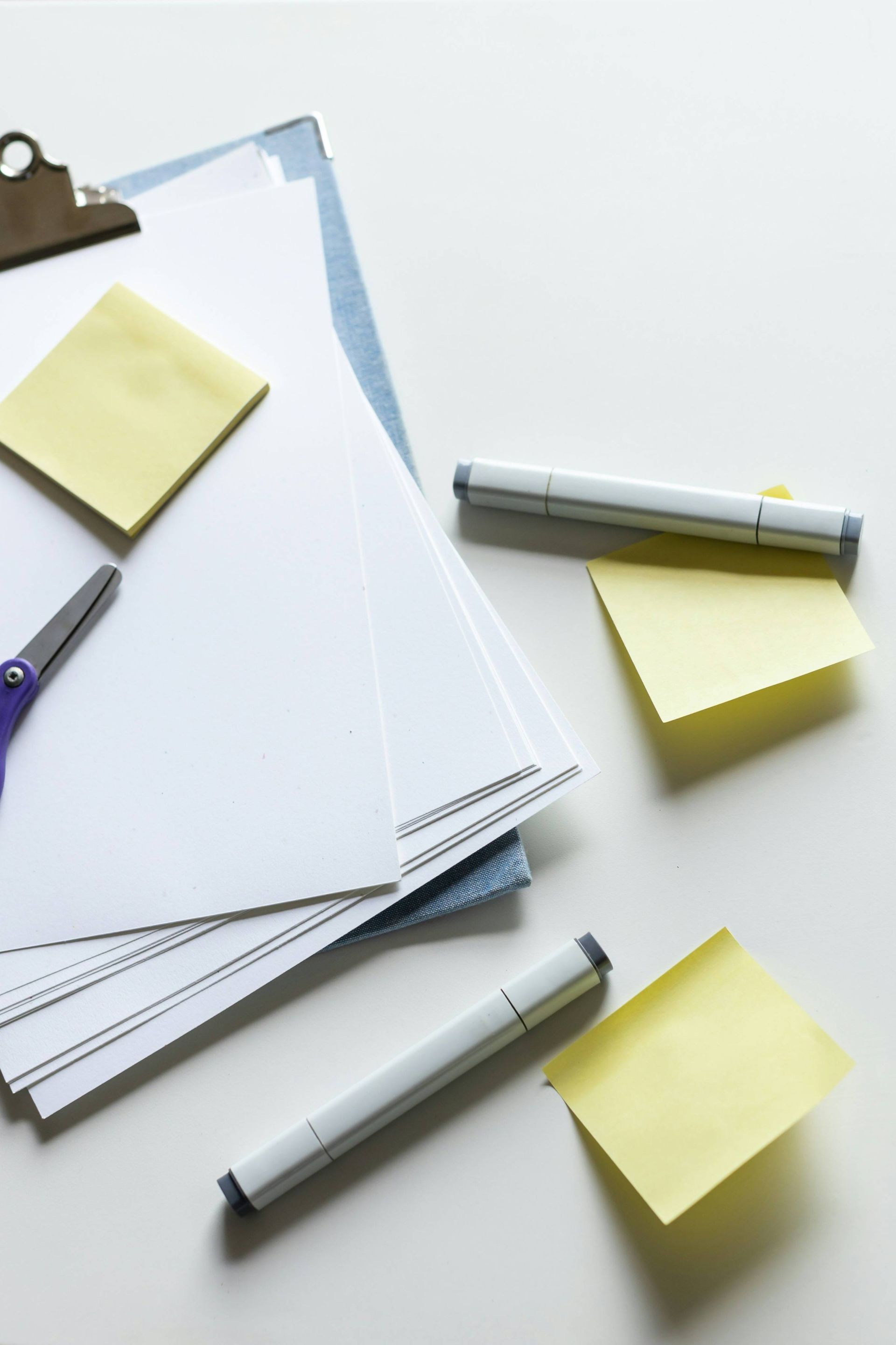 Schreibtisch mit Papierstapeln, Markern, Schere und Haftnotizen zur Vorbereitung von Notizen oder Planungen.