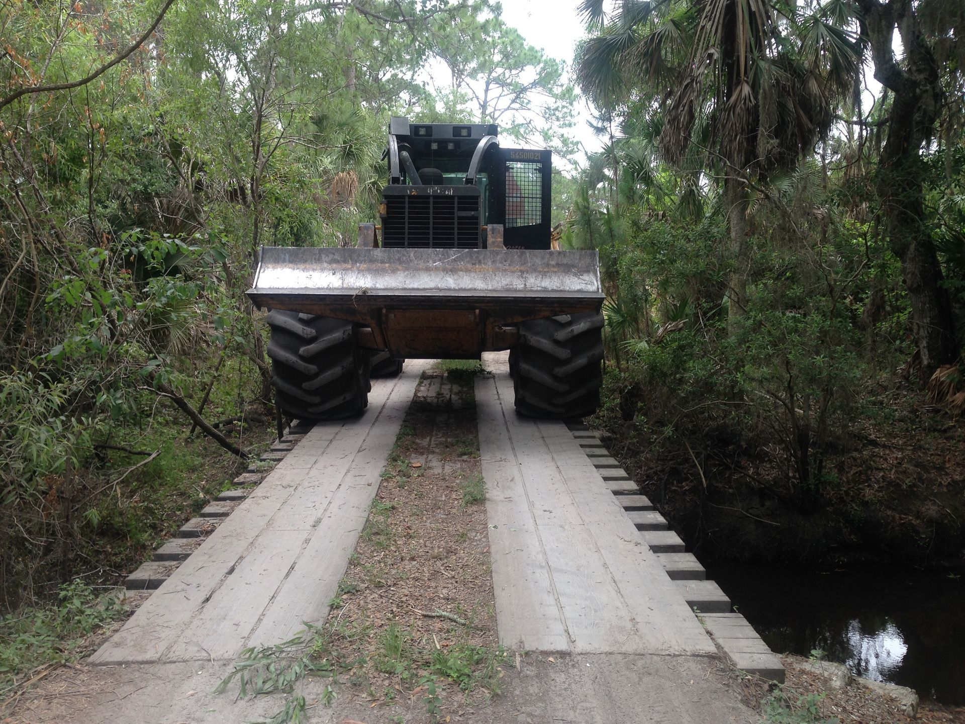 A tractor is driving over a bridge in the woods