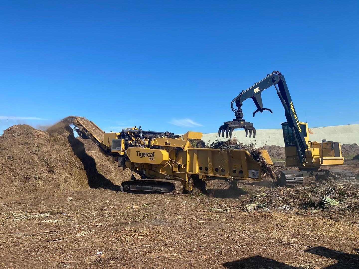 A large pile of wood chips is being loaded into a truck.