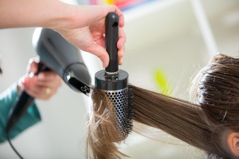 Parrucchiere che usa una spazzola rotonda e un asciugacapelli per acconciare i capelli castani.