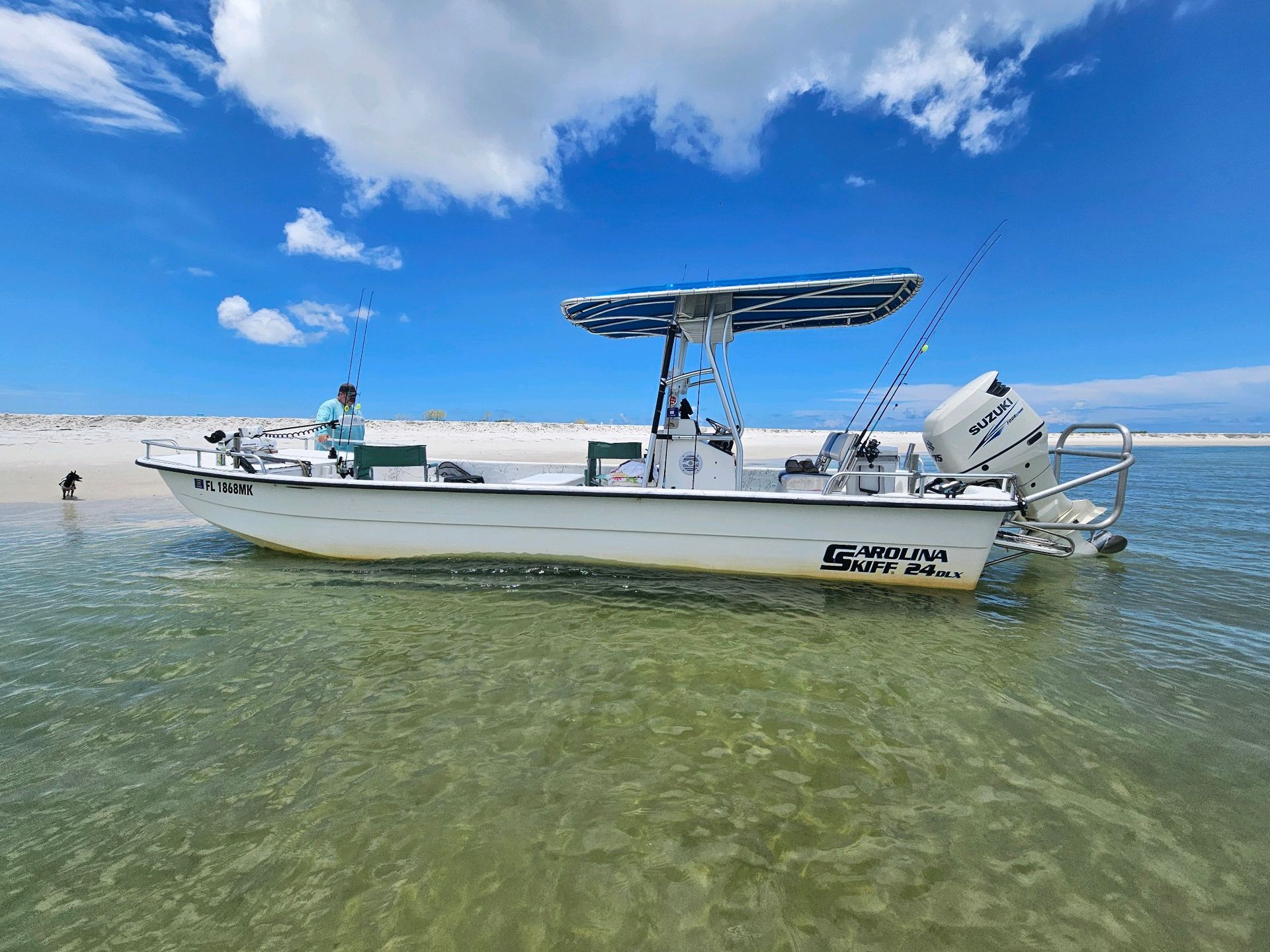 A white Carolina Skiff fishing boat anchored in shallow, clear water near a sandy beach under a bright blue sky.