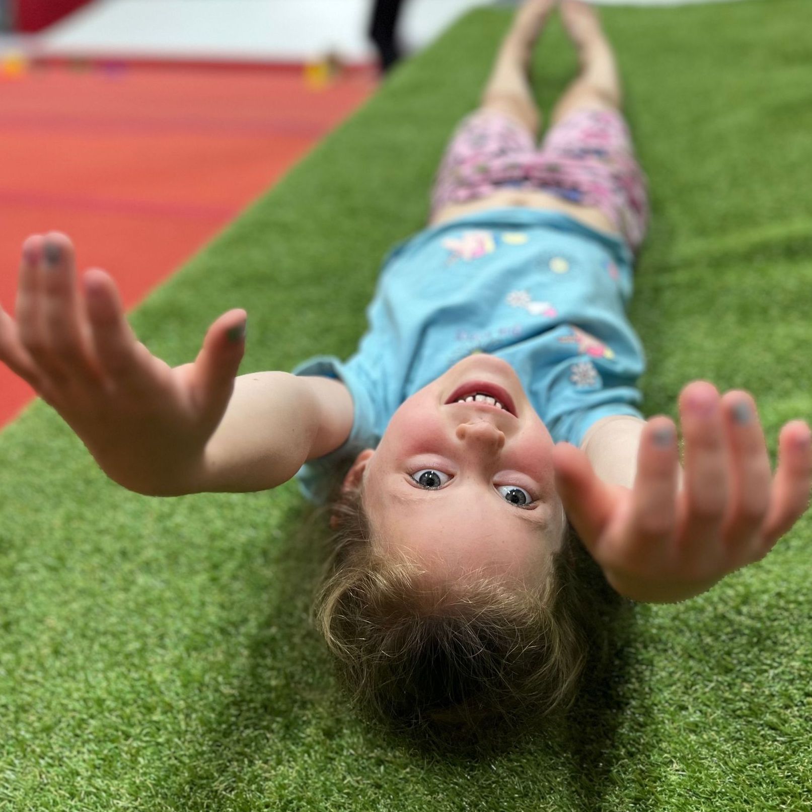 A little girl is laying on her back on the grass with her arms outstretched.