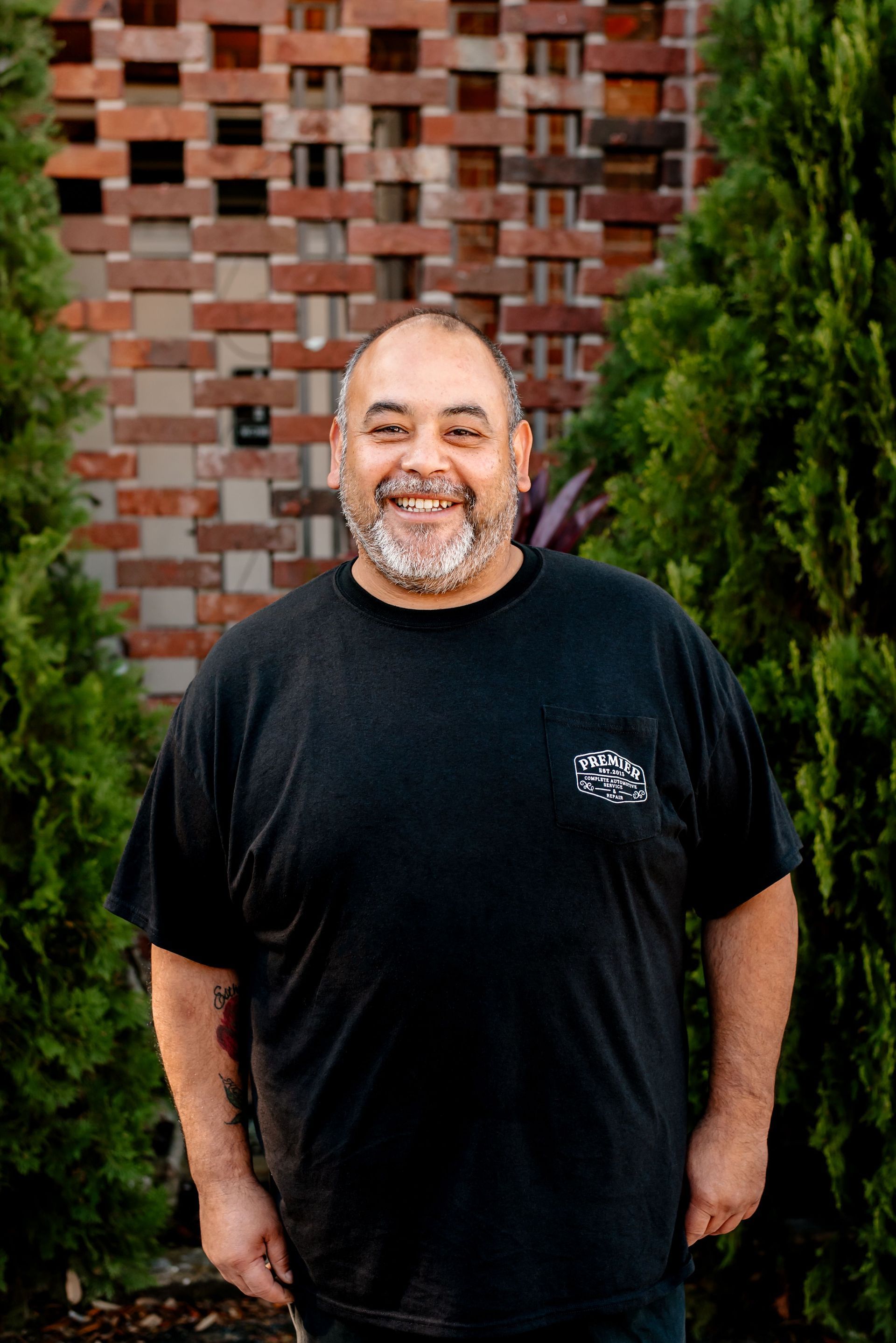 A man with a beard is standing in front of a brick wall and smiling.