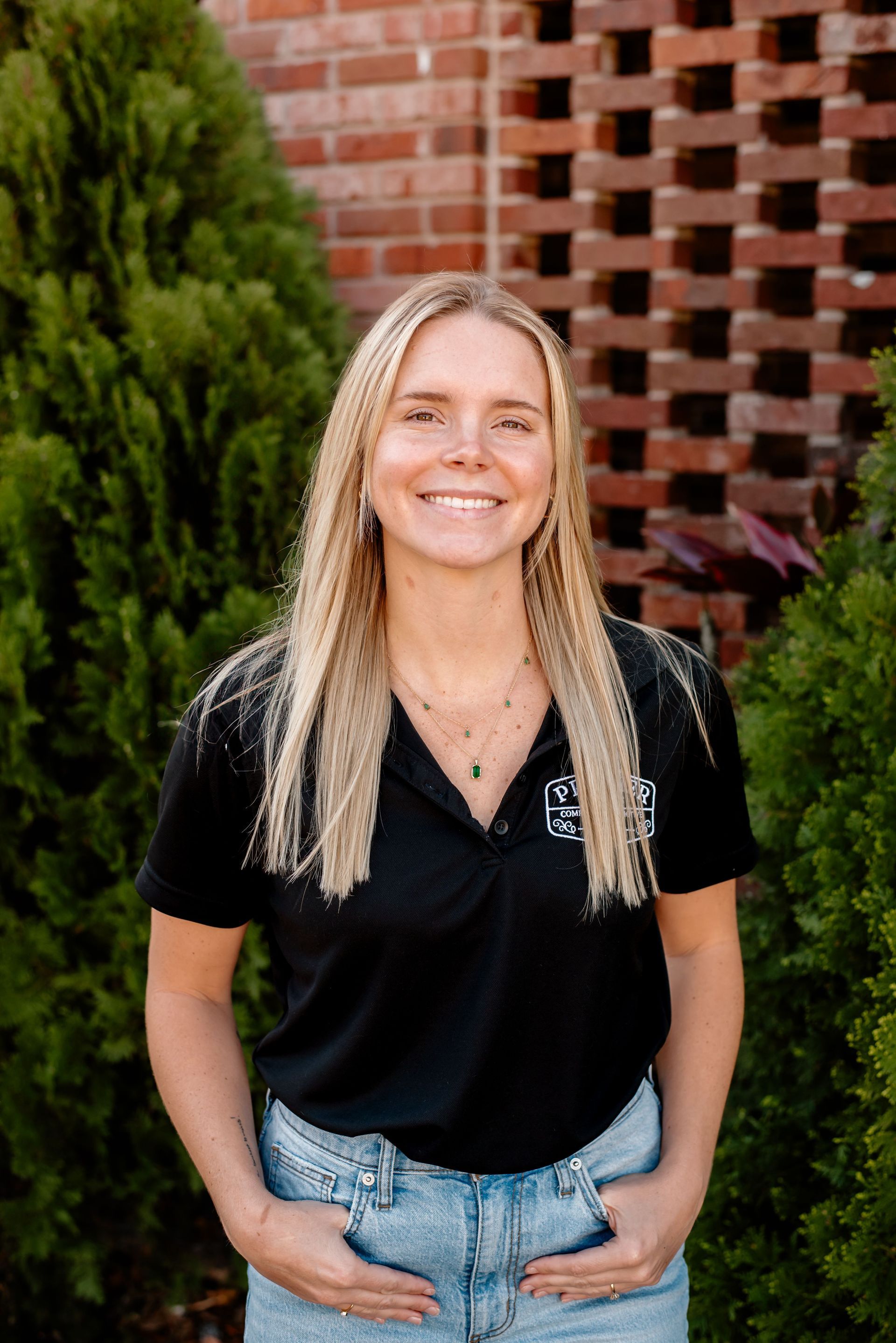 A woman in a black shirt is standing in front of a brick wall.