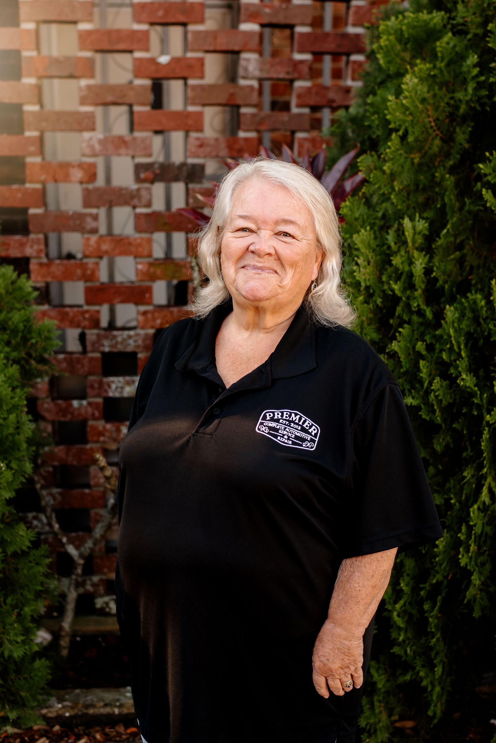 A woman in a black shirt is standing in front of a brick wall.