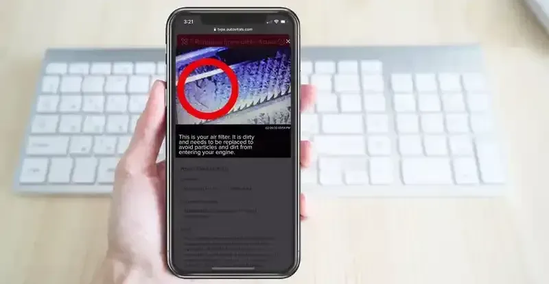 A person is holding a cell phone in front of a keyboard.