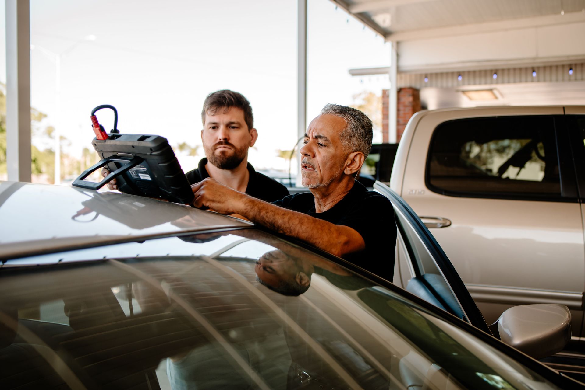 A man is looking under the hood of a car while using a tablet.