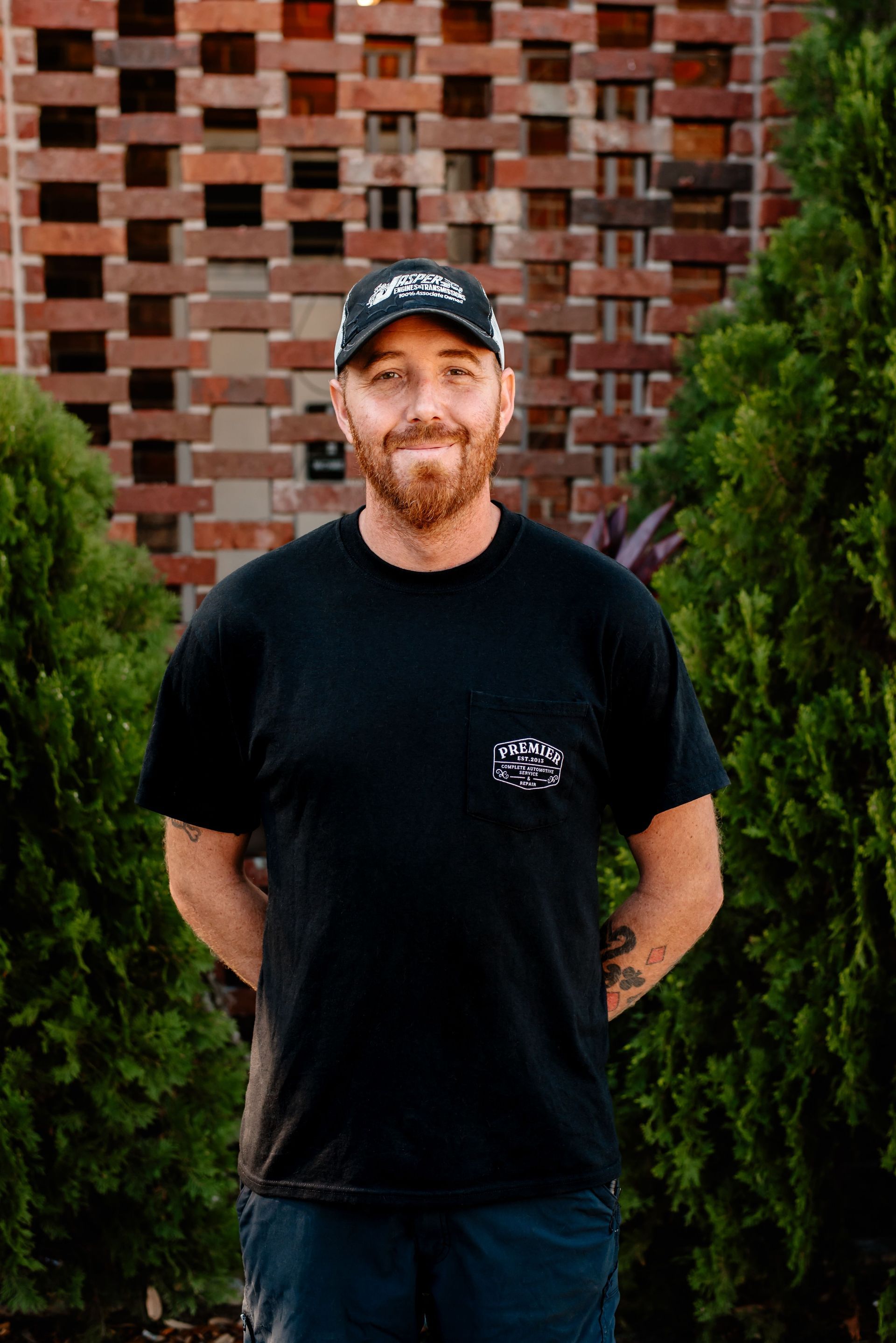 A man in a black shirt is standing in front of a brick wall.