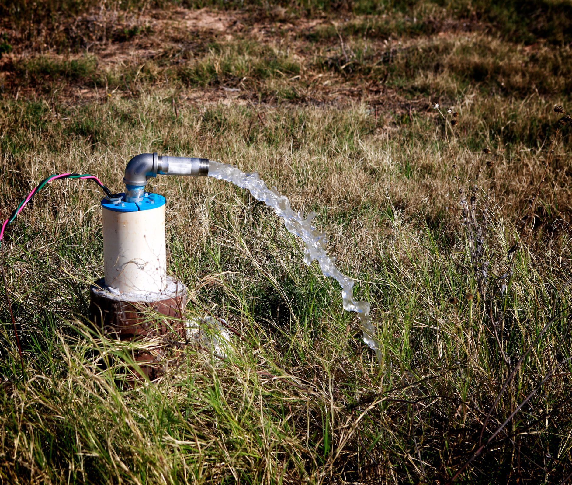 Water pump in grass, releasing water, showcasing 24-hour emergency water well repair capabilities.