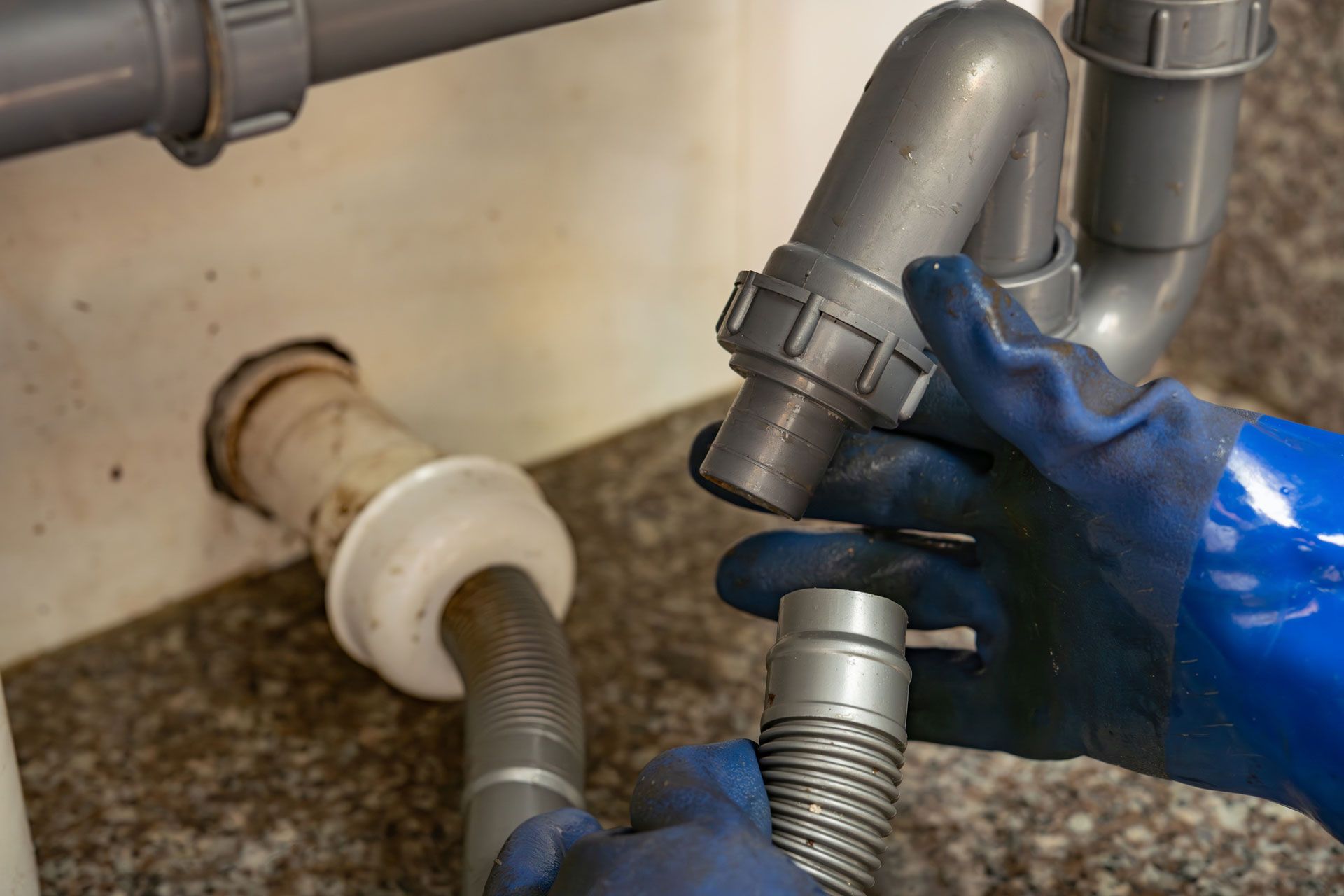 A person wearing blue gloves is fixing a sink pipe.