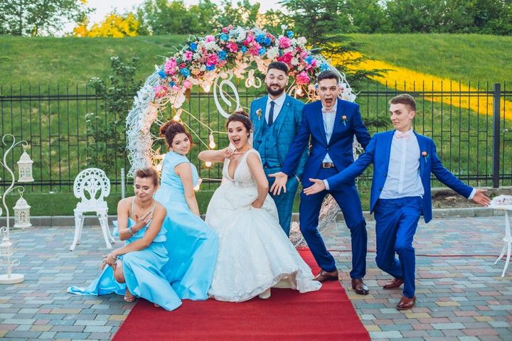 Wedding party posing on a red carpet in a garden, with the bride in white and attendants in blue suits and dresses