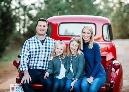 A family is sitting in the back of a red truck.