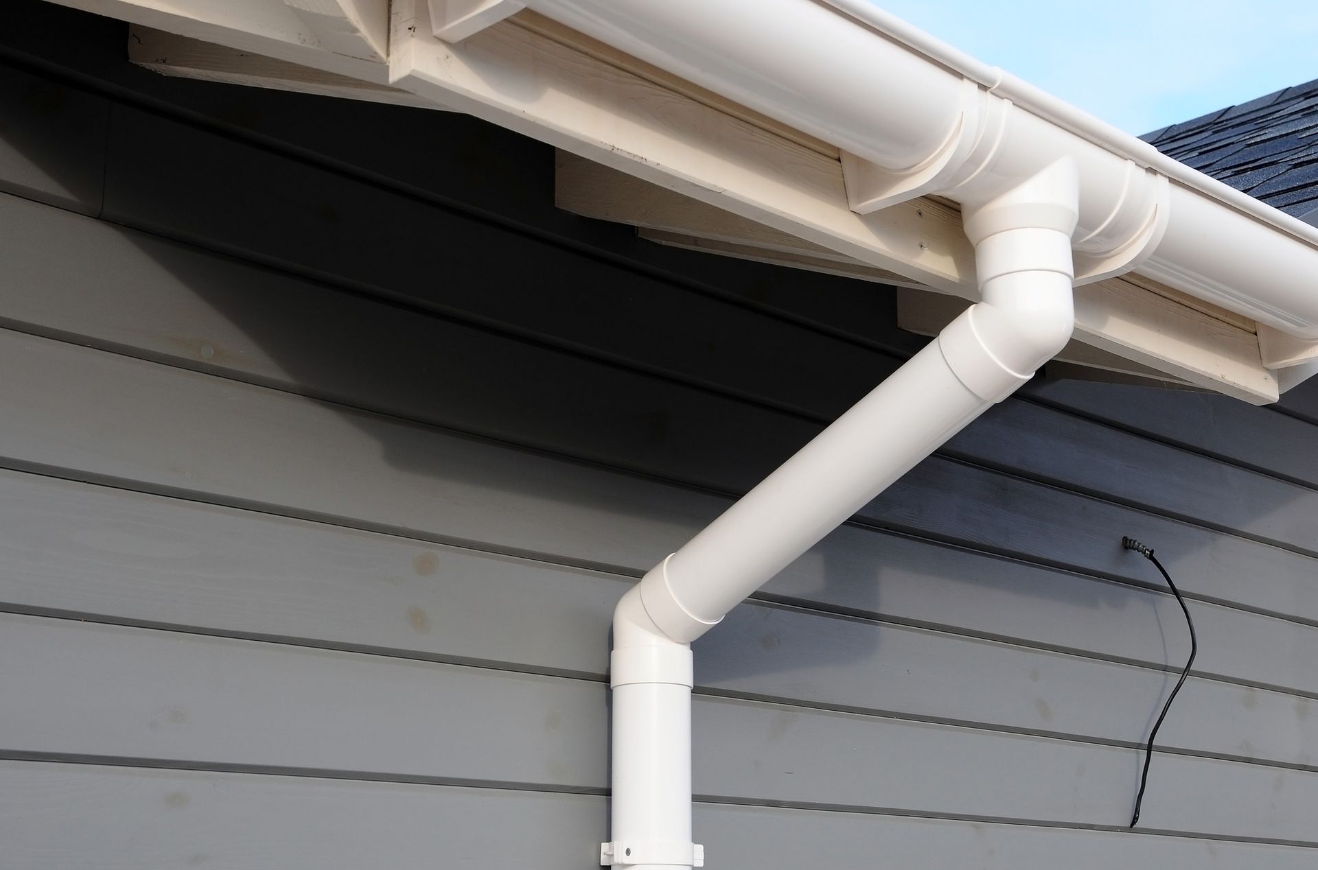 White rain gutter and downspout on a gray house, angled and connected. White rain gutter and downspout on a gray house, angled and connected.