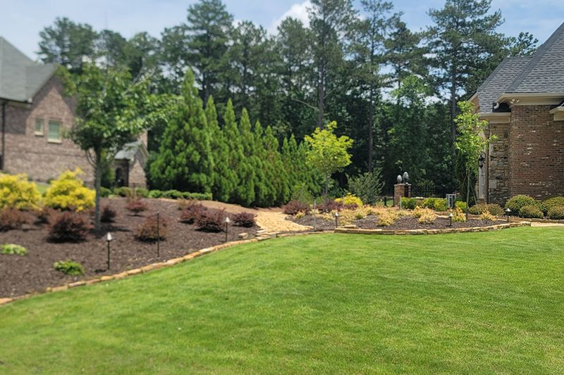 A large lawn in front of a brick house with trees in the background