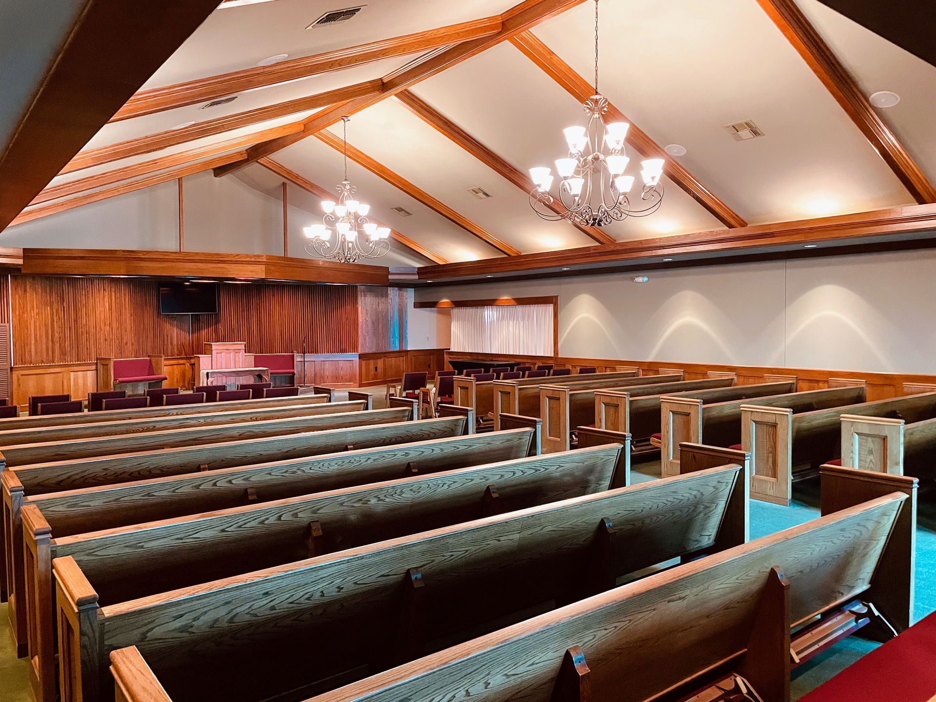 Empty church sanctuary with wooden pews, vaulted ceiling, chandeliers, and a stage at the front