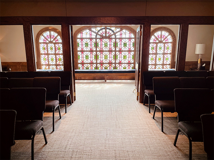 Empty church interior with pews facing stained-glass windows and a carpeted aisle