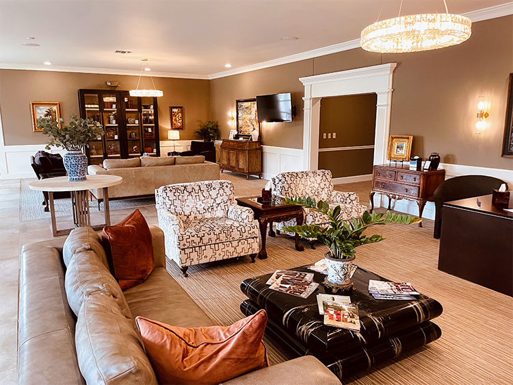 Elegant living room with beige walls, chandeliers, patterned chairs, leather sofa, and dark wood furniture.