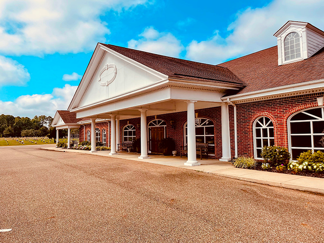 Brick building entrance with white columns, arched windows, and red roof under a blue sky