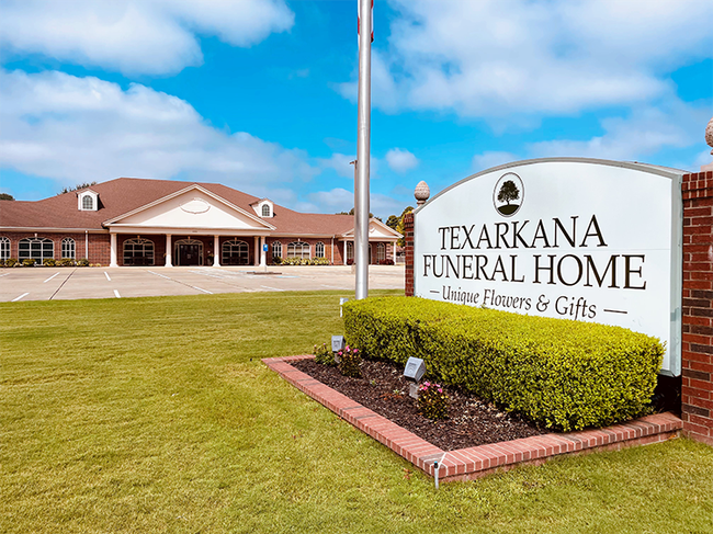 Texarkana Funeral Home sign beside a brick building and lawn under a blue sky