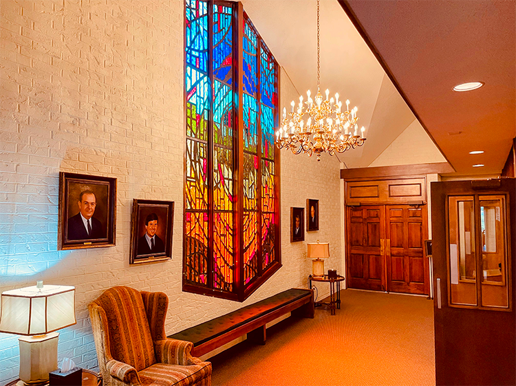 Elegant lobby with stained-glass window, chandelier, portraits, and wooden double doors