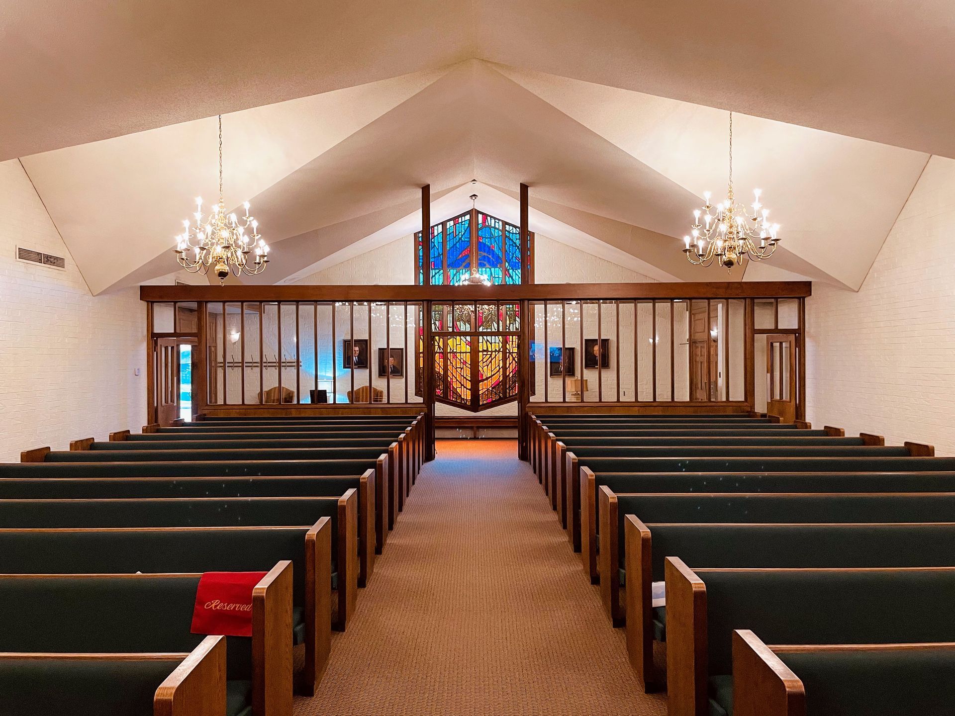 Empty church sanctuary with pews, chandeliers, stained-glass altar, and a central aisle