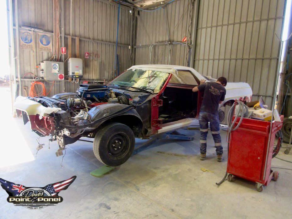 Man working on a partially disassembled classic car in a garage, preparing it for paint.