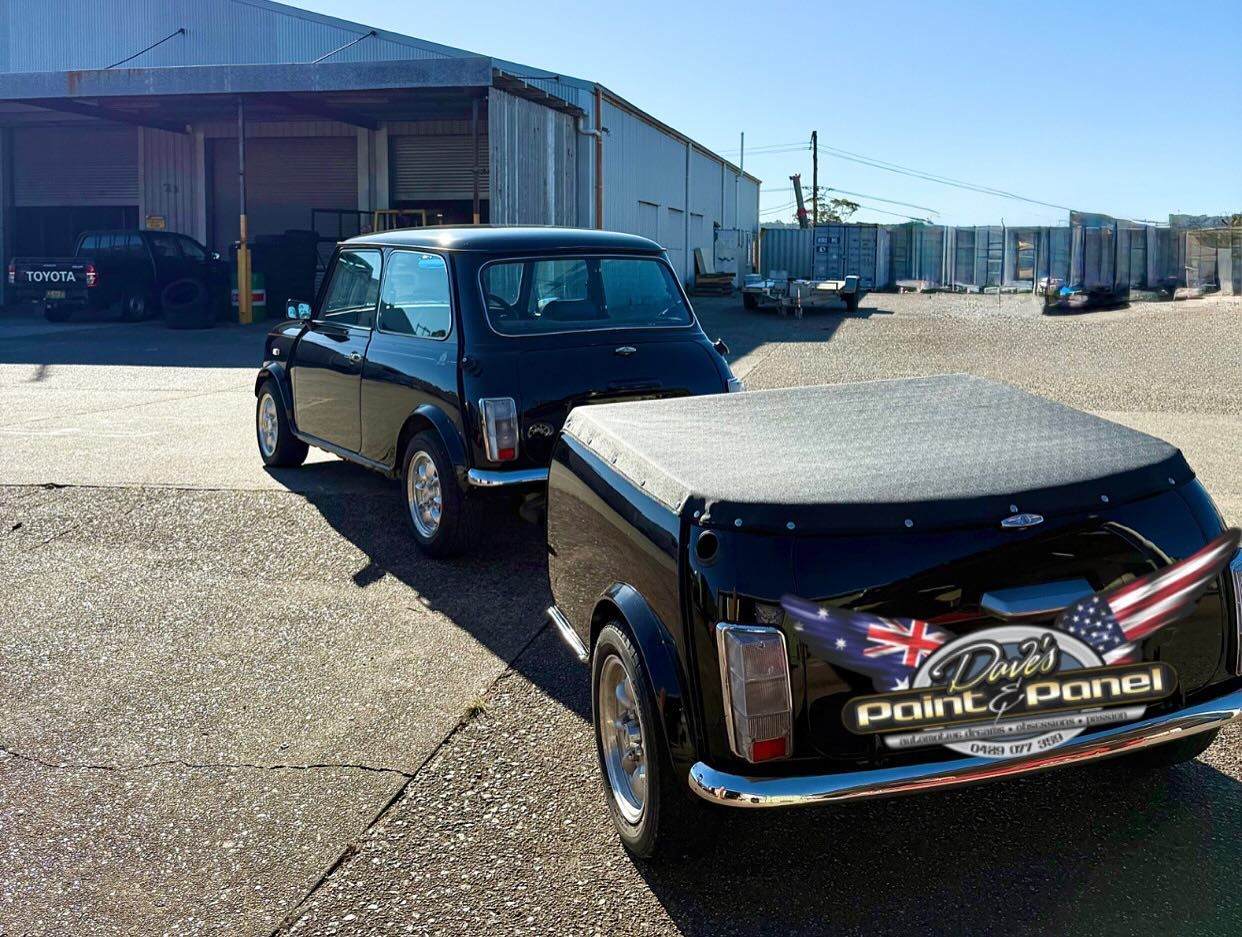 Black Mini Cooper towing a matching utility trailer; parked outdoors near a building.