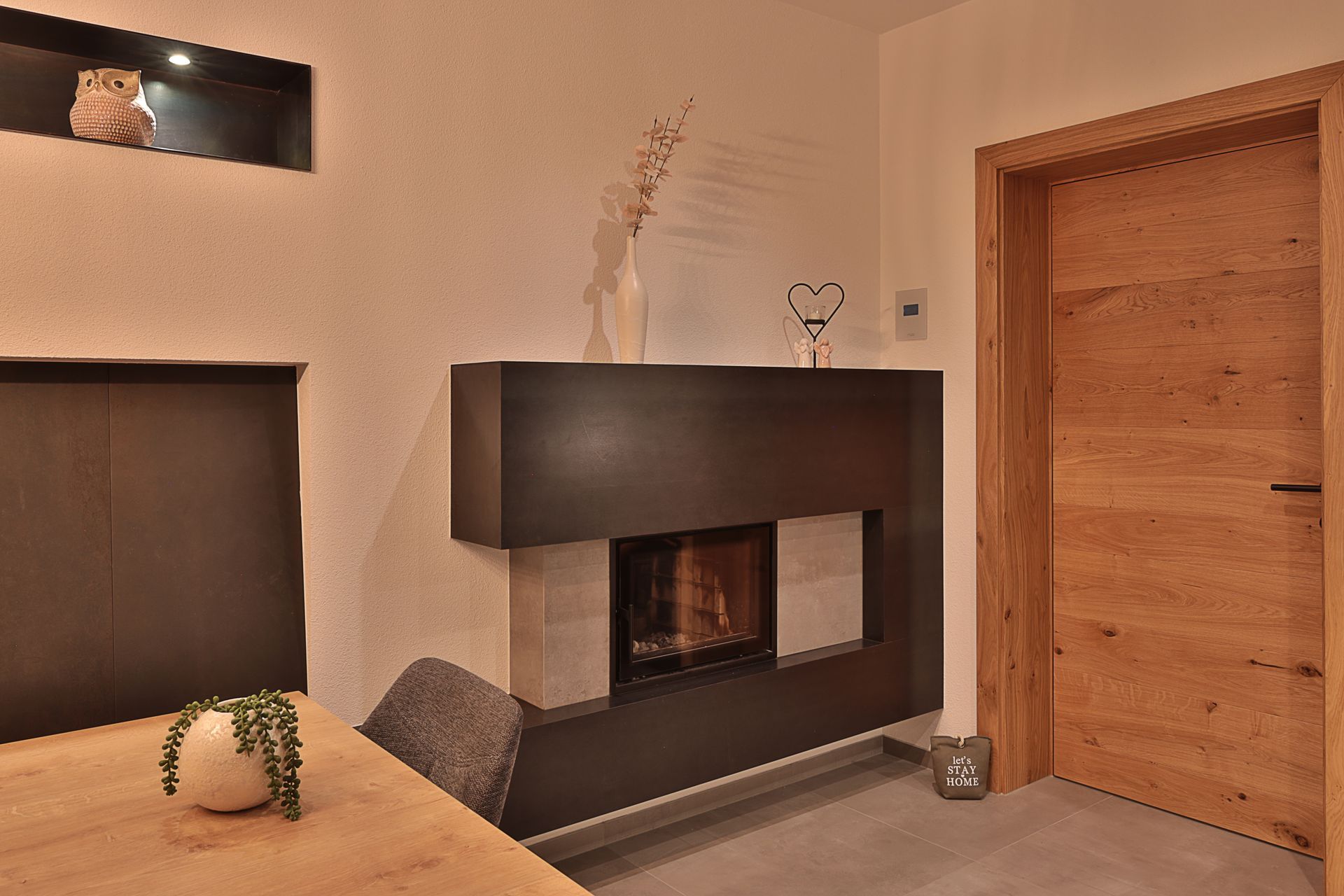 Modernes Wohnzimmer mit Kamin, Holztür und Esstisch in warmen Beigetönen.