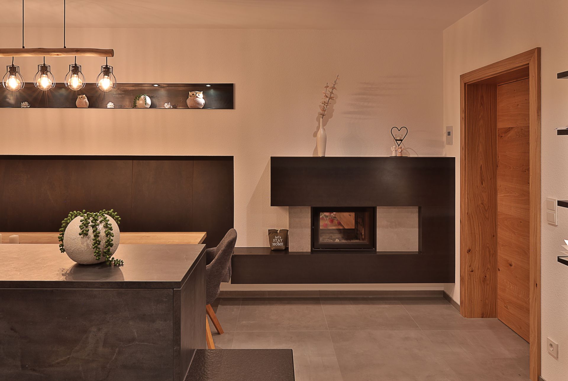 Modernes Esszimmer mit dunklem Tisch, Pendelleuchten, eingebauter Sitzbank und einer Kaminnische