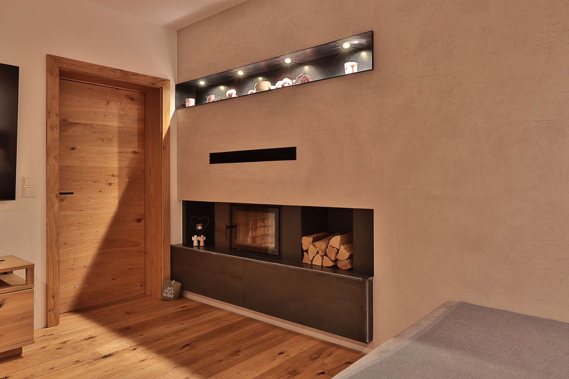 Modernes Wohnzimmer mit Holzboden, Kamin und warmem, eingelassenem Licht darüber.