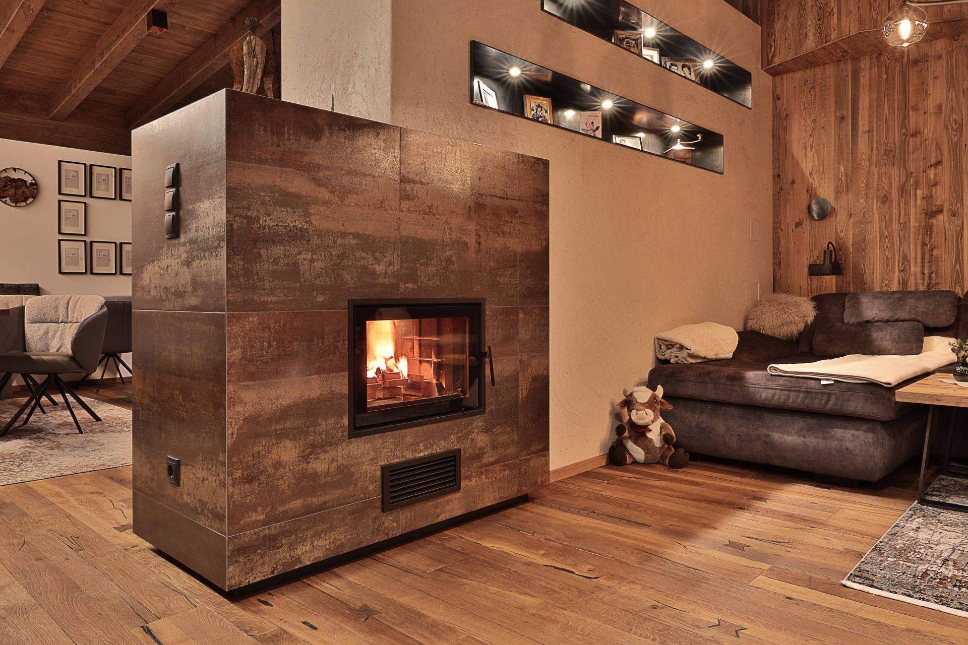 Modernes Wohnzimmer im Landhausstil mit beleuchtetem Kamin, holzgetäfelten Wänden und einem dunklen Sofa.