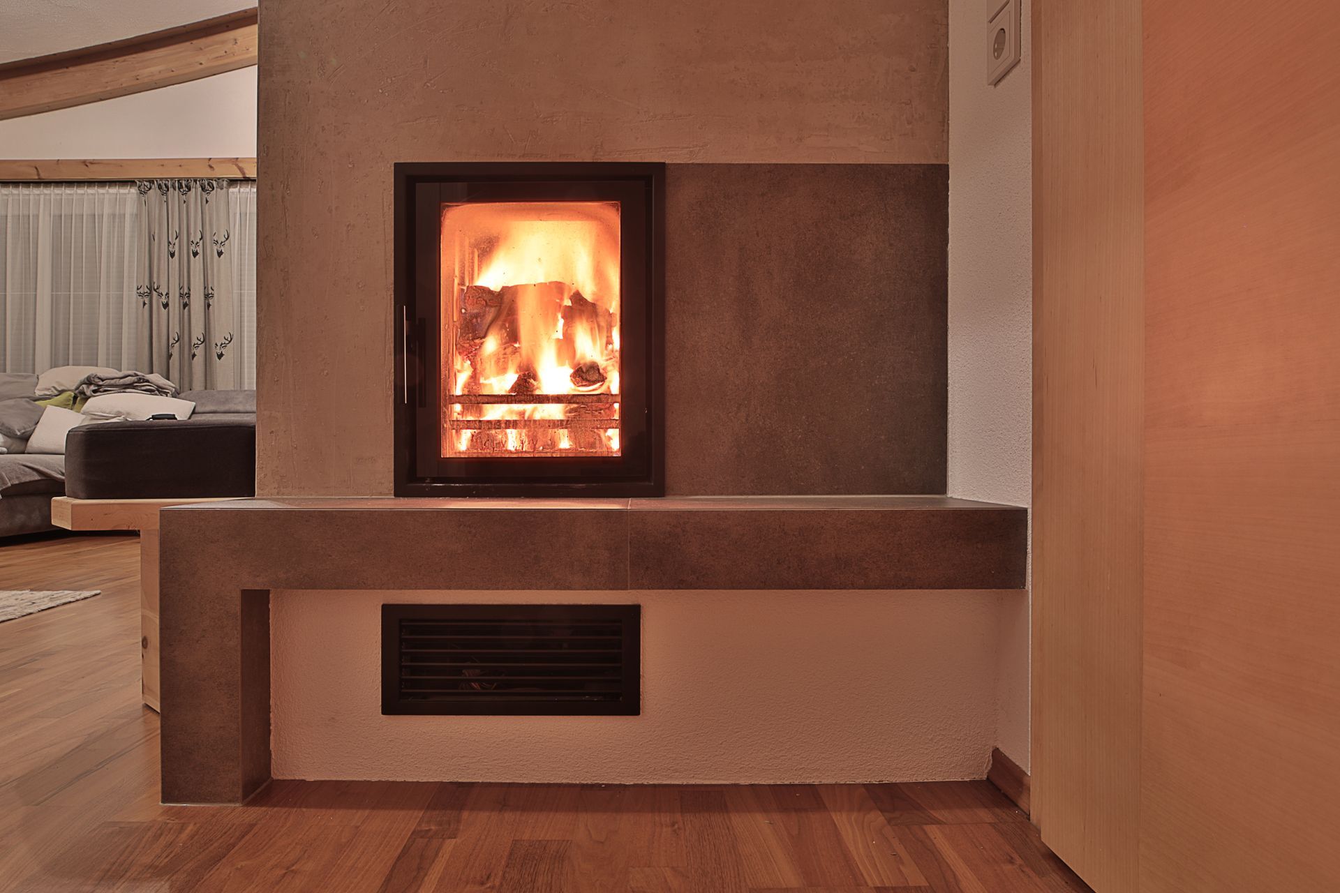 Modernes Wohnzimmer mit einem in eine braune Wand eingelassenen, beleuchteten Kamin und Holzboden.