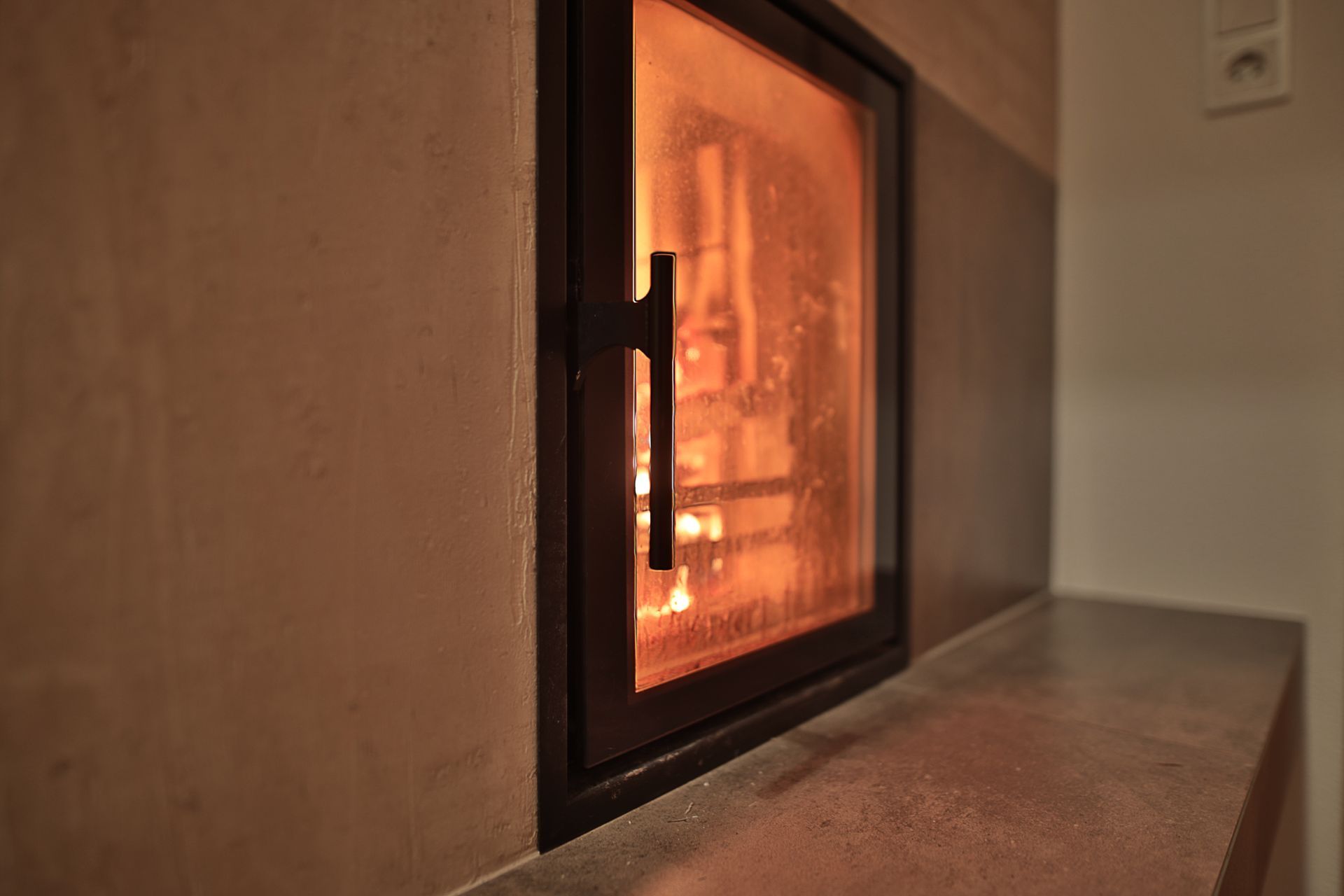 Ein Kamin mit Glasfront, der in einem beigen Raum orange leuchtet.
