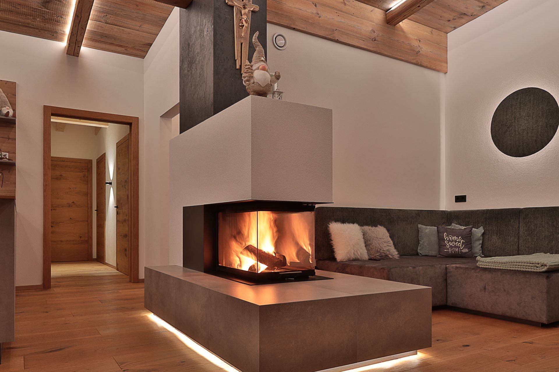 Modernes Wohnzimmer mit beleuchtetem Kamin, grauem Sofa, Holzbalken und warmem Licht