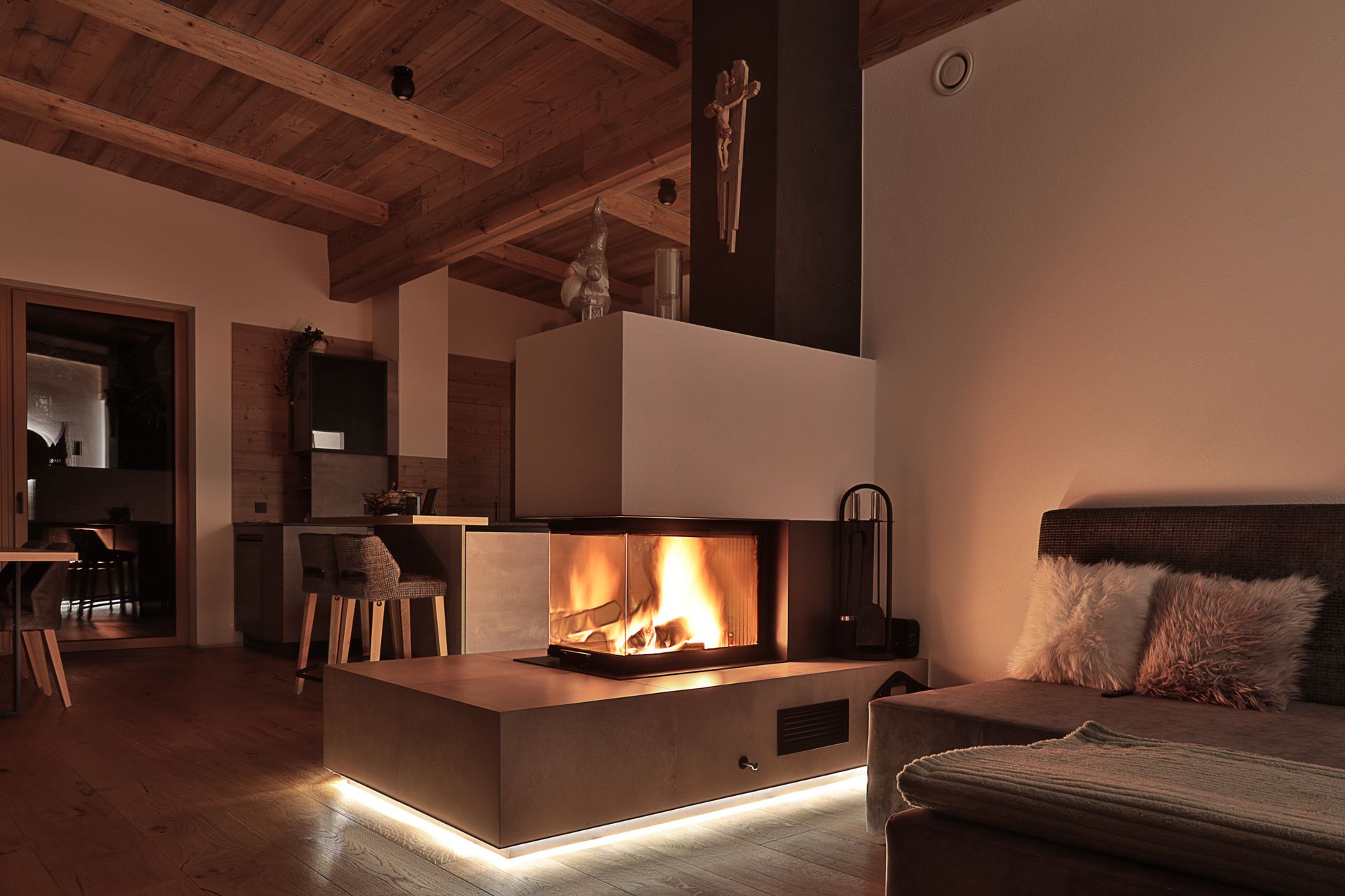 Gemütliches, modernes Wohnzimmer mit beleuchtetem Kamin, Holzbalken an der Decke und einem gepolsterten Sofa.